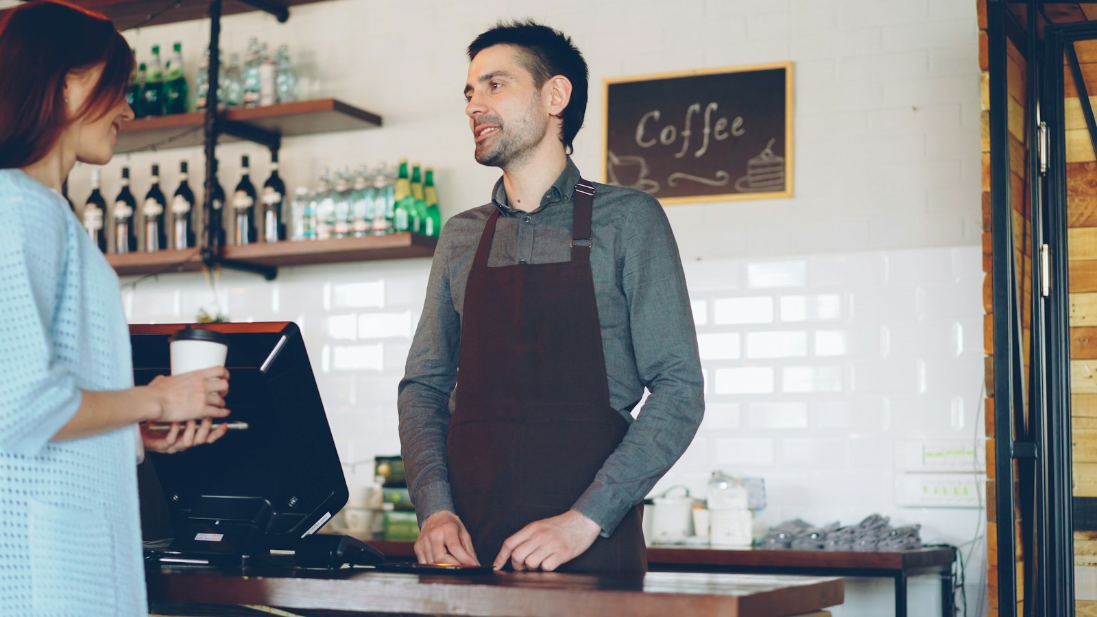 A café worker talking with a customer holding a takeaway coffee